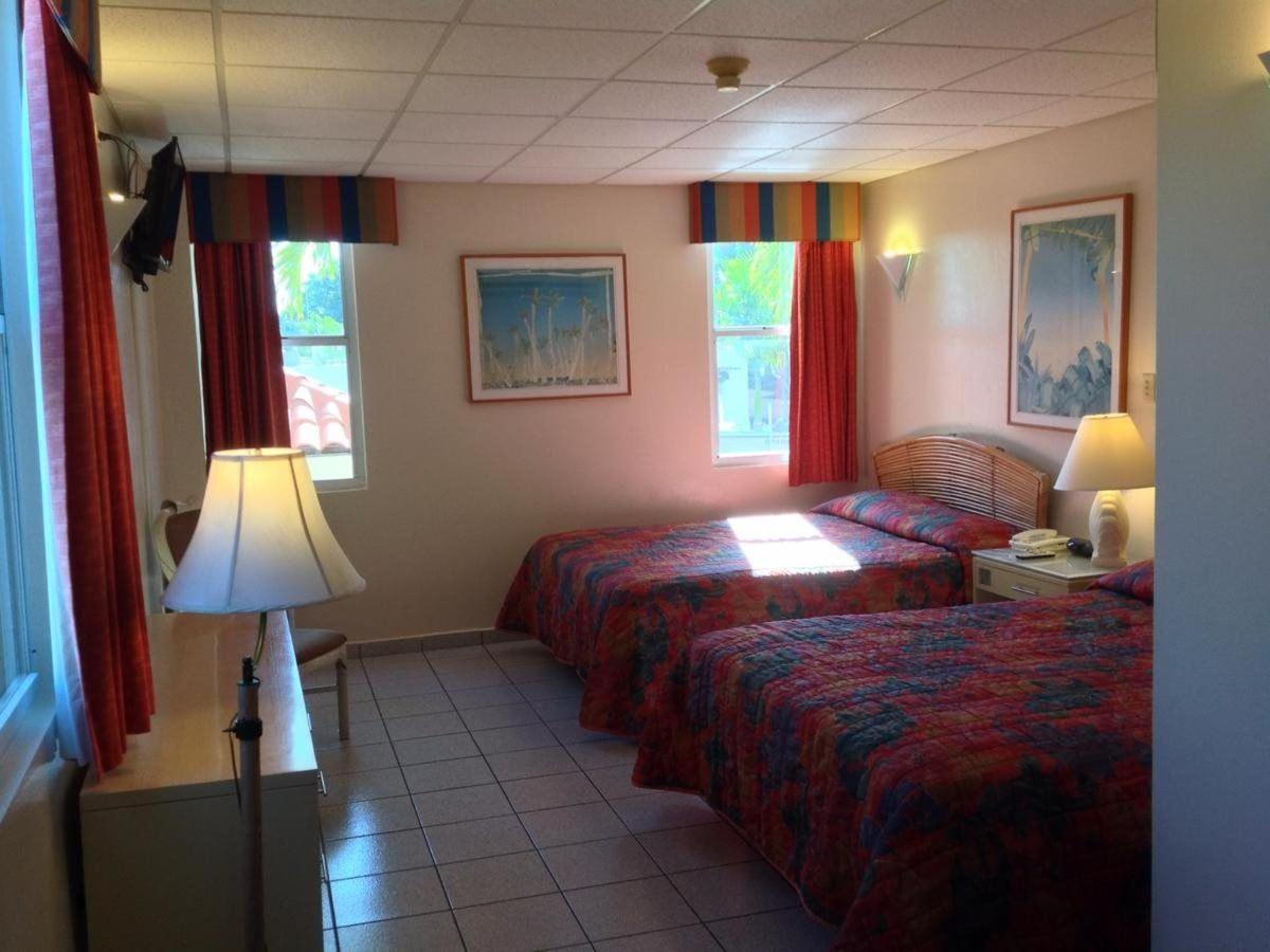 Hotel room with two beds featuring floral bedspreads, red curtains, tiled floor, and framed wall art
