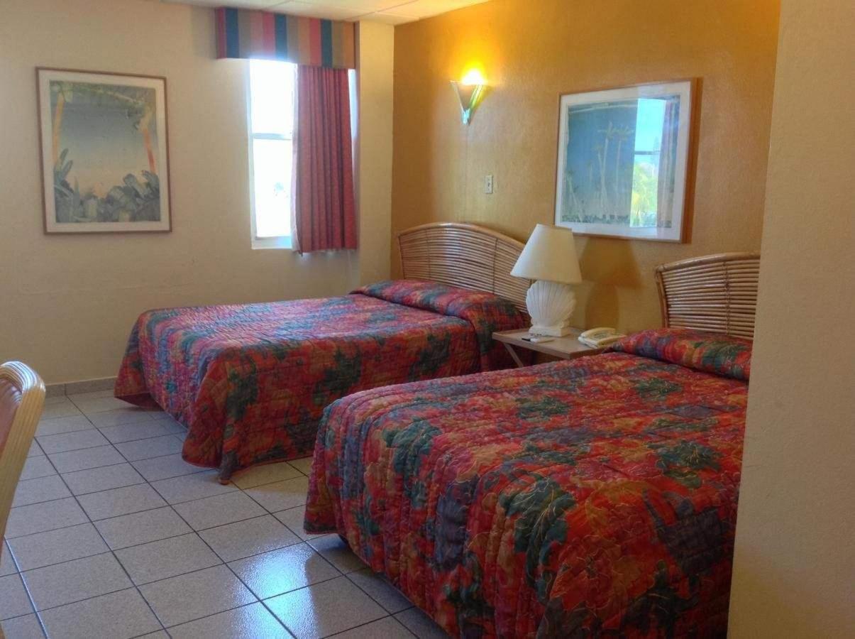 Hotel room with two floral-patterned beds, rattan headboards, tile floor, and warm orange walls